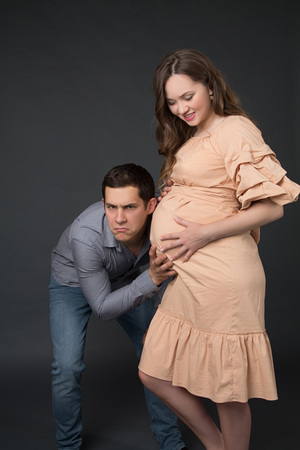 pregnant woman in a beige dress with her husband standing on the gray backgroundの写真素材