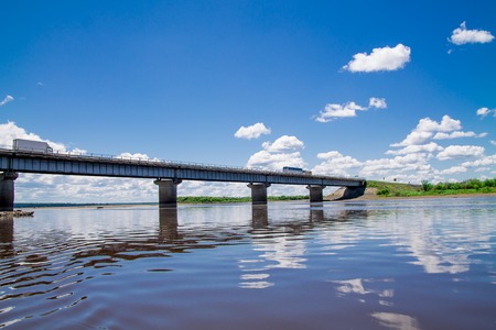 steel bridge with lots of fluffy clouds in the bright blue sky and their reflection on still water like in a mirrorの写真素材