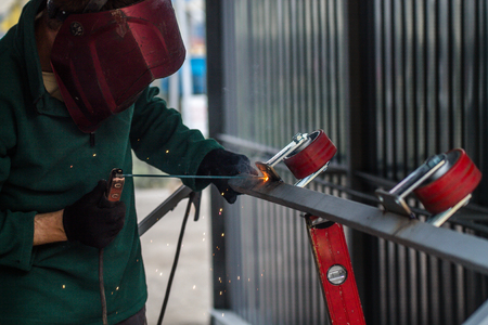welder is welding metal part with lots of sparks and smoke on a dark metal backgroundの写真素材