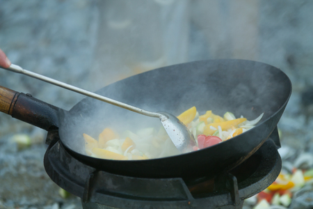 cooking fresh vegetables outdoors in a wok on open fireの写真素材