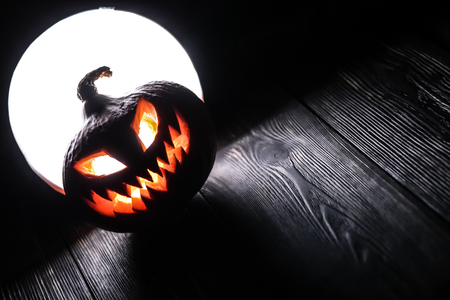 Halloween pumpkin Jack-o-lantern on the dark wooden background with a scary face as a symbol of halloween night with the concept full moon behind it.の写真素材