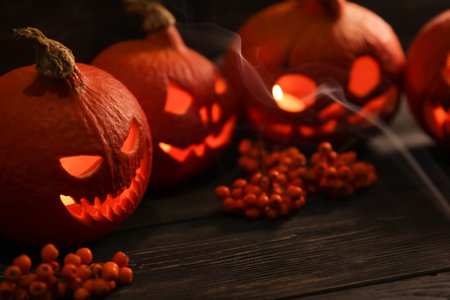 scary halloween pumpkin lanterns with luminous scary faces with rowanberries on a wooden background and the clouds of smoke in front of themの写真素材