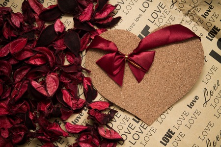 cork heart with red ribbon among red rose petals layed on craft paperの写真素材