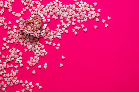 Love and marriage concept. Valentine's Day. Two golden wedding rings lying in a metal heart among lots of fair pink small hearts on a pink background with a copy space.の写真素材