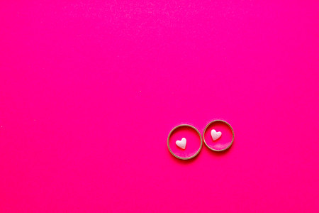 Love and marriage concept. Valentine's Day. Two golden wedding rings with small light pink hearts within on a bright pink background with copy spaceの写真素材