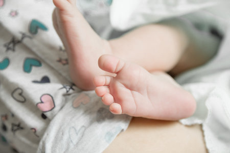 Little soft newborn baby feet on mother's hands in white clothes