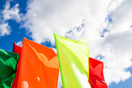 Colorful red and yellow flags waving on the bright blue sky background with white fluffy clouds