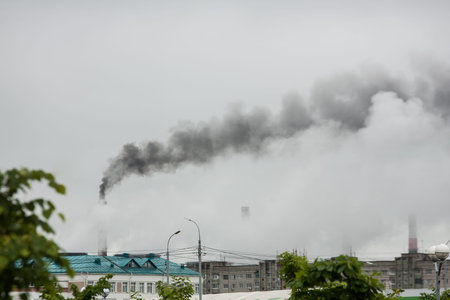 industrial chimneys with heavy smoke causing the air pollution during foggy weather with green...
