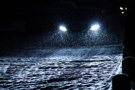 the snowflakes during snowfall lit with light from car headlights at night on a road