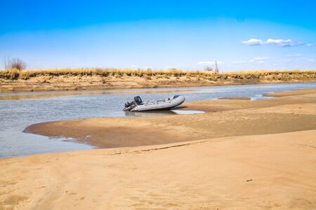 River motor boat near a sandy river bank with golden dunes and blue waterの写真素材
