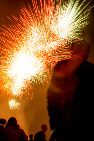 Silhouettes of people watching yellow, white and red fireworks in night sky on Independence Day