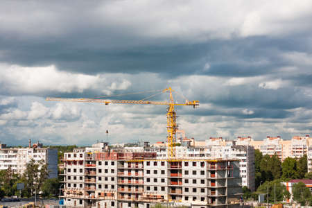 Construction crane on construction site in city on cloudy sky backgroundの写真素材