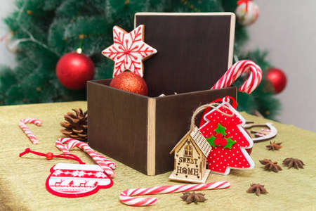 dark brown wooden copy space in a Christmas gift composition with festive decoration, gingerbread and sugar cane candies in a dark brown box on golden surface with Chrismas tree on background. Happy New Year 2021の写真素材