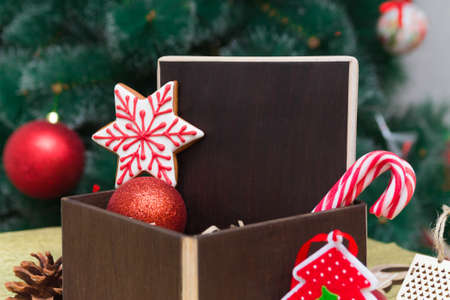 dark brown wooden copy space in a Christmas gift composition with festive decoration, gingerbread and sugar cane candies in a dark brown box on golden surface with Chrismas tree on background. Happy New Year 2021の写真素材