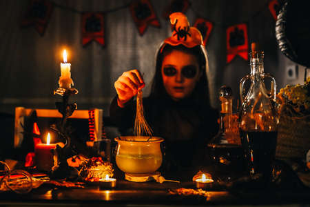 Little girl witch making magic potion at Halloween night with candles around her. Horror.の写真素材