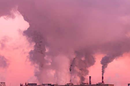 industrial chimneys with heavy smoke causing air pollution as ecological problem on pink sunset sky backgroundの写真素材