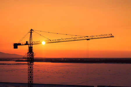 silhouette of tower crane with the sun behind it during the orange sunsetの写真素材