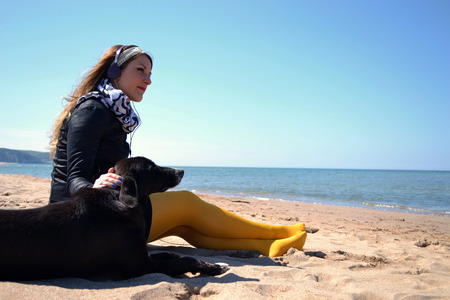 unhappy woman sitting on the beach with the dogの写真素材