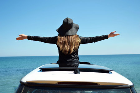 Rear view of relaxed woman on summer travel vacation to the coast towards the sea leaning out the...