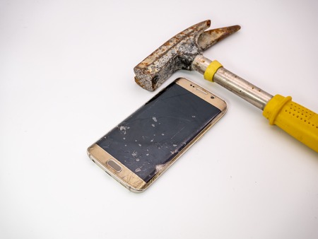 damaged smartphone disply with hammer next to itの写真素材