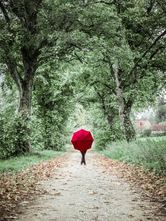 Abstract setting of a Woman with red umbrella posing in the autumn landscapeの写真素材