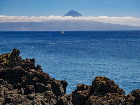Image from a cliff with a sailing boat in the atlantic and the island of Pico with mountain Pico in the background Azores Portugal Europeの写真素材
