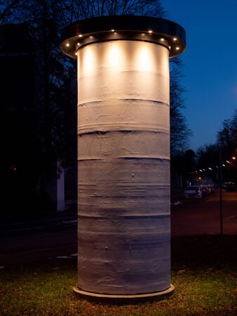 Image of Photo enlighted blank white mockup poster of street advertising column stand on grasの写真素材