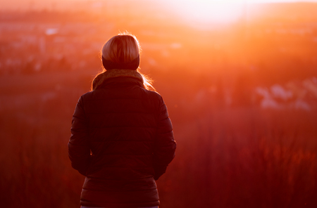 Image of woman from behind looking into the sun during colorful sunsetの写真素材