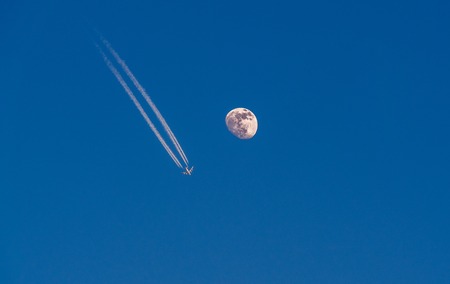 Image of airplane with condensation trails flying next to the detailed moonの写真素材