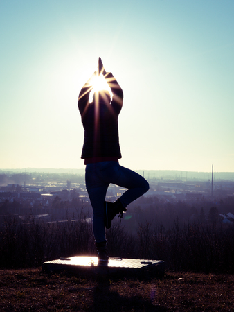 Image of womans silhouette performing a yoga tree on a platform with sun raysの写真素材