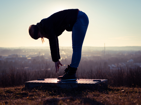 Image of womans silhouette performing gymnastics on a platform with sun raysの写真素材