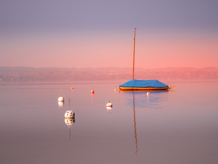 Image of mothballed sailing boat on a lake with water reflections during sunset on lake Ammer, Bavaria, Germanyの写真素材
