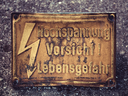 Image of an old yeloow warning sign with flash and german words Hochspannung Vorsicht Lebensgefahr, which means Danger High Voltageの写真素材