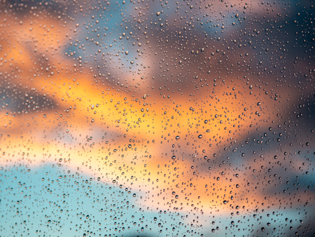 Image of window with rain drops and colorful clouds in the background during sun setの写真素材