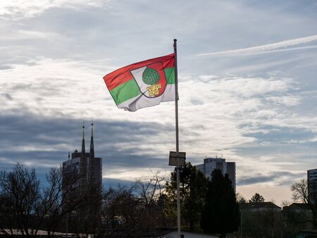 Augsburg, Germany - December 15, 2019: Illuminated flag of the soccer club FC Augsburg flatters in the wind with stormy dark clouds and the cityscape of Augsburg in the backgroundのeditorial素材