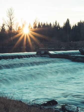 Water flowing over a weir during sunset with sun rays in the winter, Augsburgの写真素材