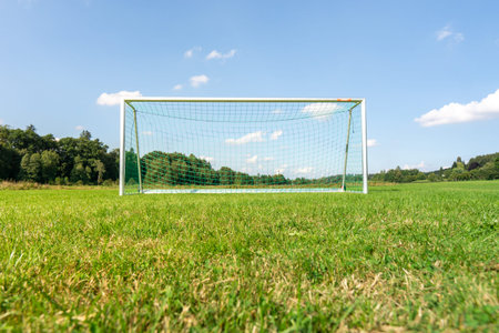 Focus on green grass of a football field with blurry goal in the background.の写真素材