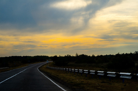 Long highway at sunset. Trees, grass, clouds. Anyone. Horizontal photoの写真素材