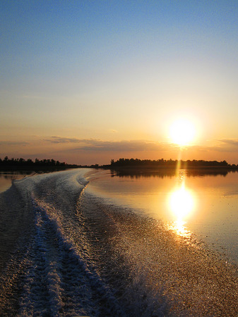 Track on the water from the powerboat. Water, trees. Nobody. The reflection of the sun on the water. Sunsetの写真素材