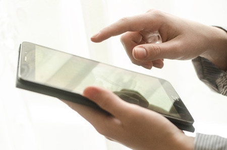 Women's hands are holding a tablet against the windowの写真素材