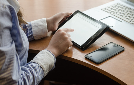 Woman in shirt sitting with a tablet. Sitting at a table, on a table, and cup a smartphone and laptopの写真素材