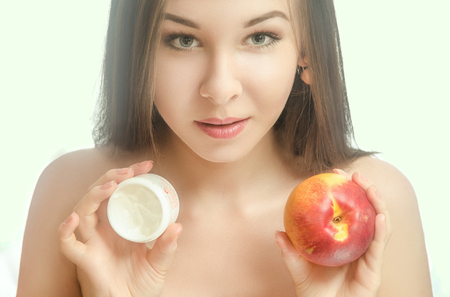 Young tender woman with her hair holding a peach and cream. White backgroundの写真素材