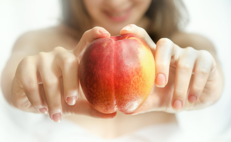 Peach in female hands. White background. Blurred image of smiling girl. Horizontal photoの写真素材
