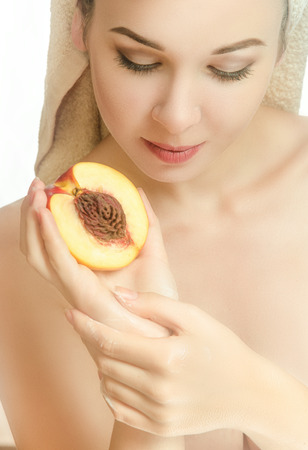 Woman with half a peach and a towel on his head. With cream on hand. Beauty. Vertical photoの写真素材