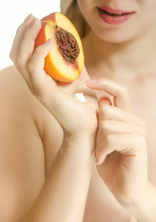 Half of peach in female hands. Cream on hand. Vertical photoの写真素材