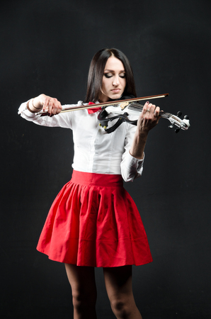 Young woman in a red skirt and a blouse playing the violin. On a black background. Vertical photoの写真素材