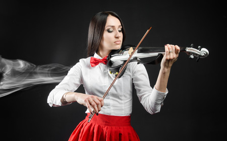 Attractive  woman playing the violin on a black background and smokeの写真素材