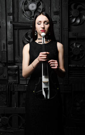 Portrait of a young woman with a violin. In a black dress. Hands holding a violin. Closed eyesの写真素材