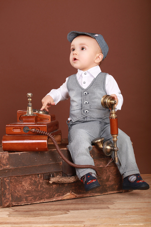 Cute baby sitting on a suitcase, holding a vintage phone and looking upの写真素材