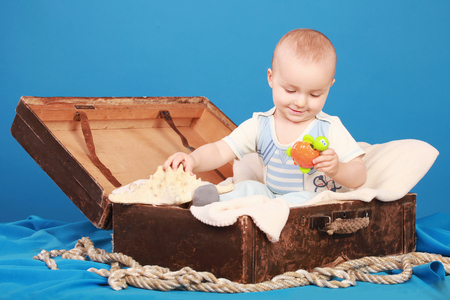 A cute baby sits in a chest in a sailor suit and looks at a toy turtleの写真素材